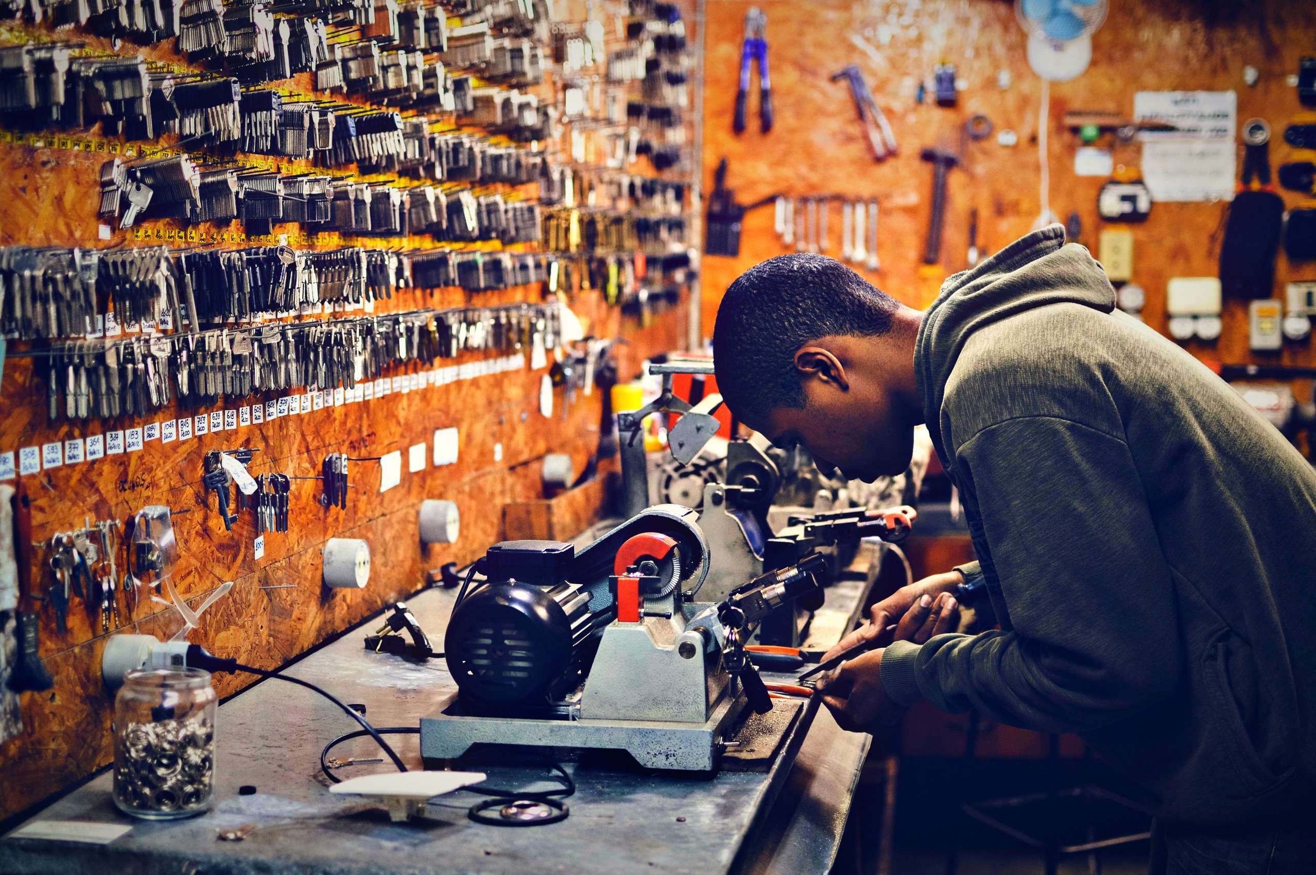 Technician cutting a car key on a key-cutting machine in a workshop lined with key blanks